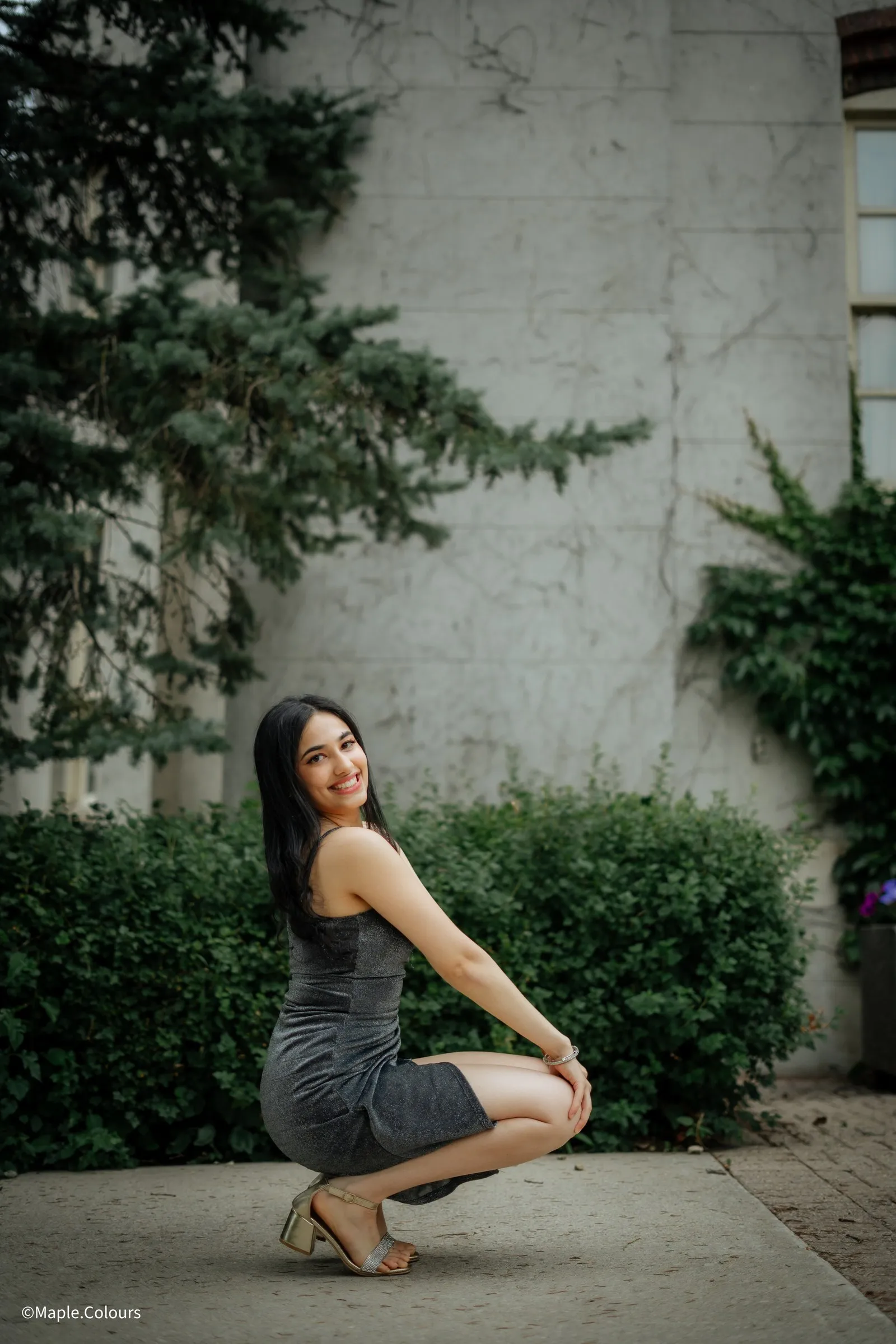 Fashion portrait crouching against a garden hedge
