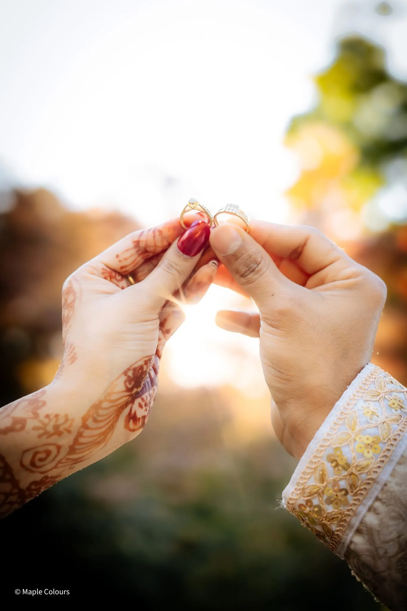 Wedding rings held to the setting sun between henna-painted hands