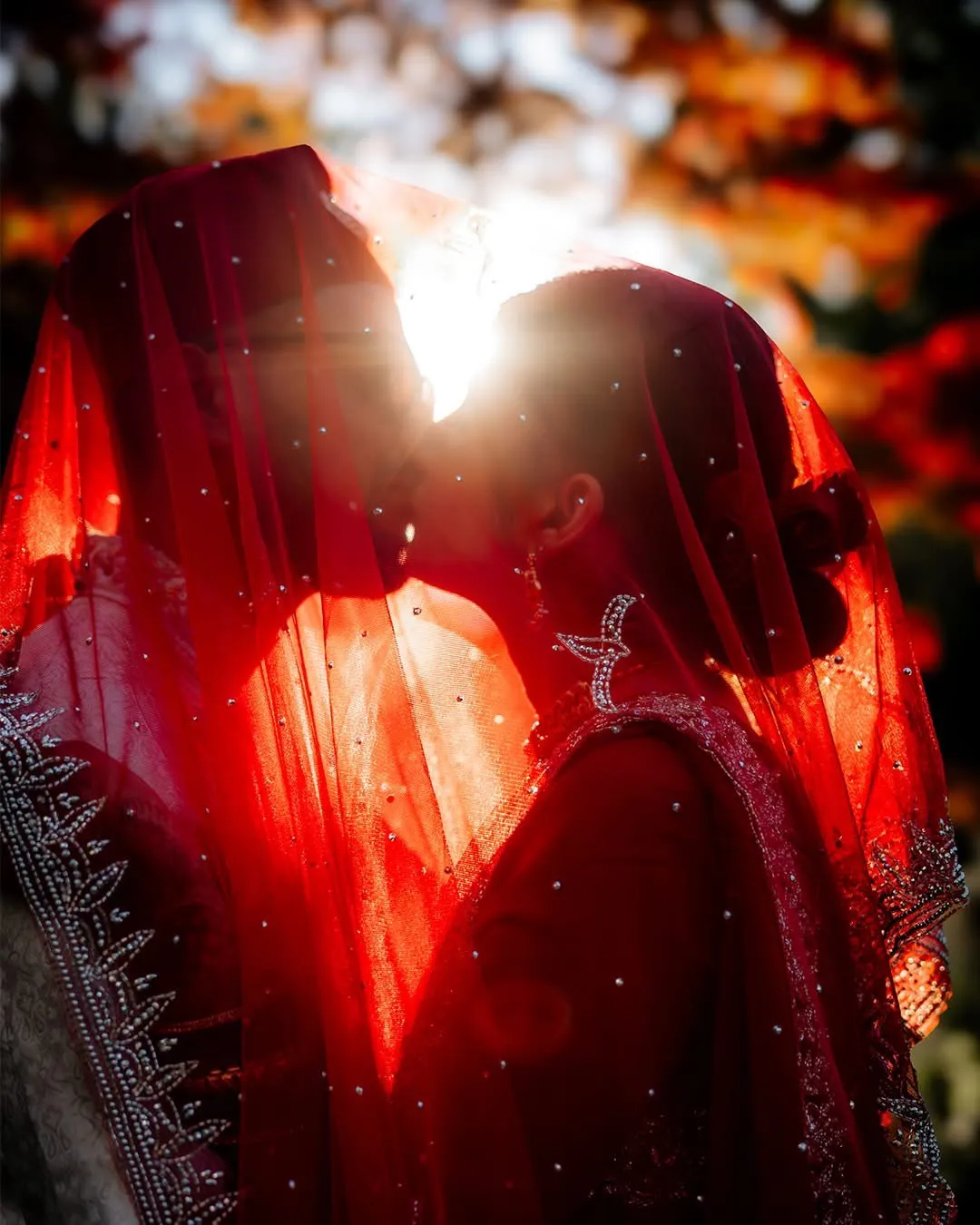 Couple backlit beneath a red bridal veil