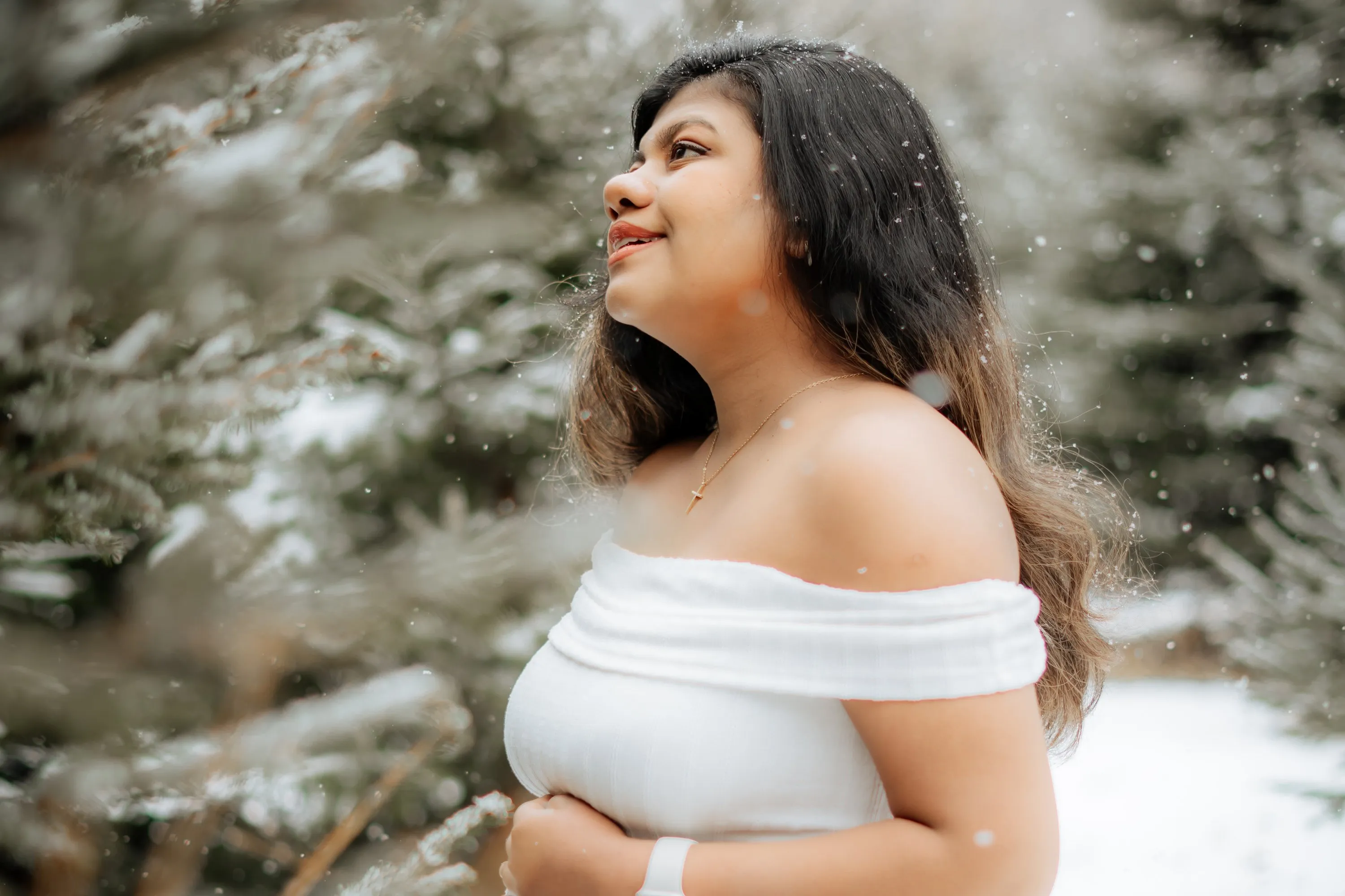 Maternity portrait in falling snow among winter pines